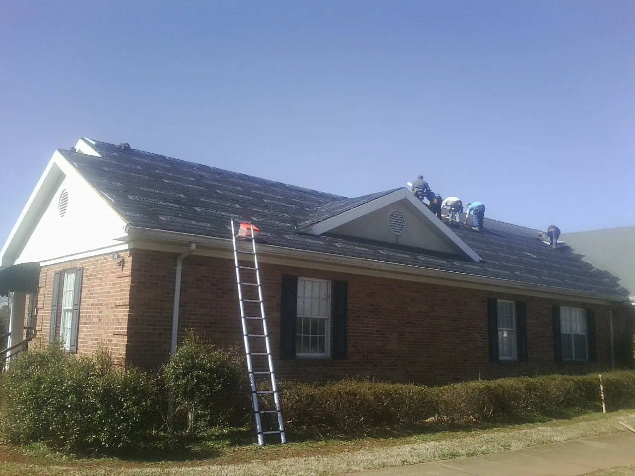 Crew tearing shingles off a brick ranch roof with a ladder set — Emergency Roof Repair work by our crew in Perkinsville