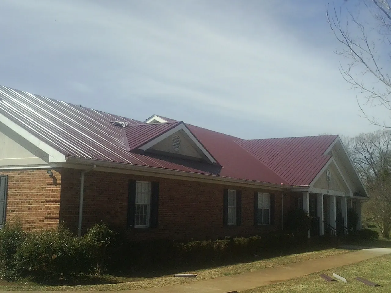 Red metal roof with gabled entries on a long brick building, from a Hail Damage Roof Repair job in Perkinsville