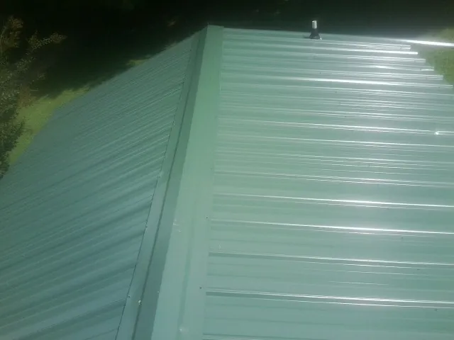 New green metal panels meeting at the ridge of a roof — Flat Roof Repair work by our crew in Perkinsville