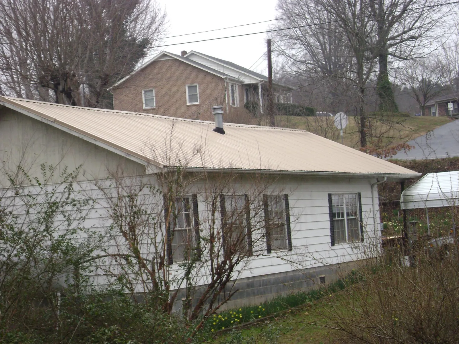 Tan metal roof on a white sided house set into a hillside — Commercial Roofing by Roofing Brothers in Perkinsville